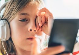 Tired Little girl with headphones using smart phone and rubbing eyes